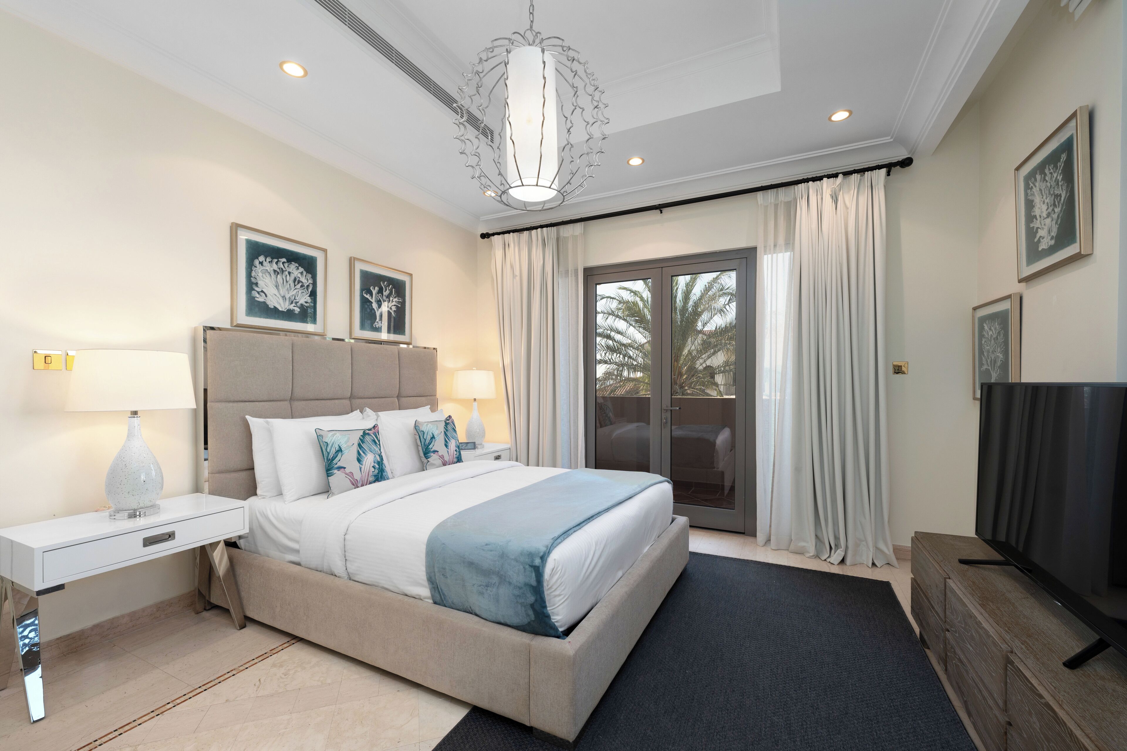 Quarto de hotel moderno com uma cama grande, televisão de tela plana, escrivaninha e varanda com cortinas.