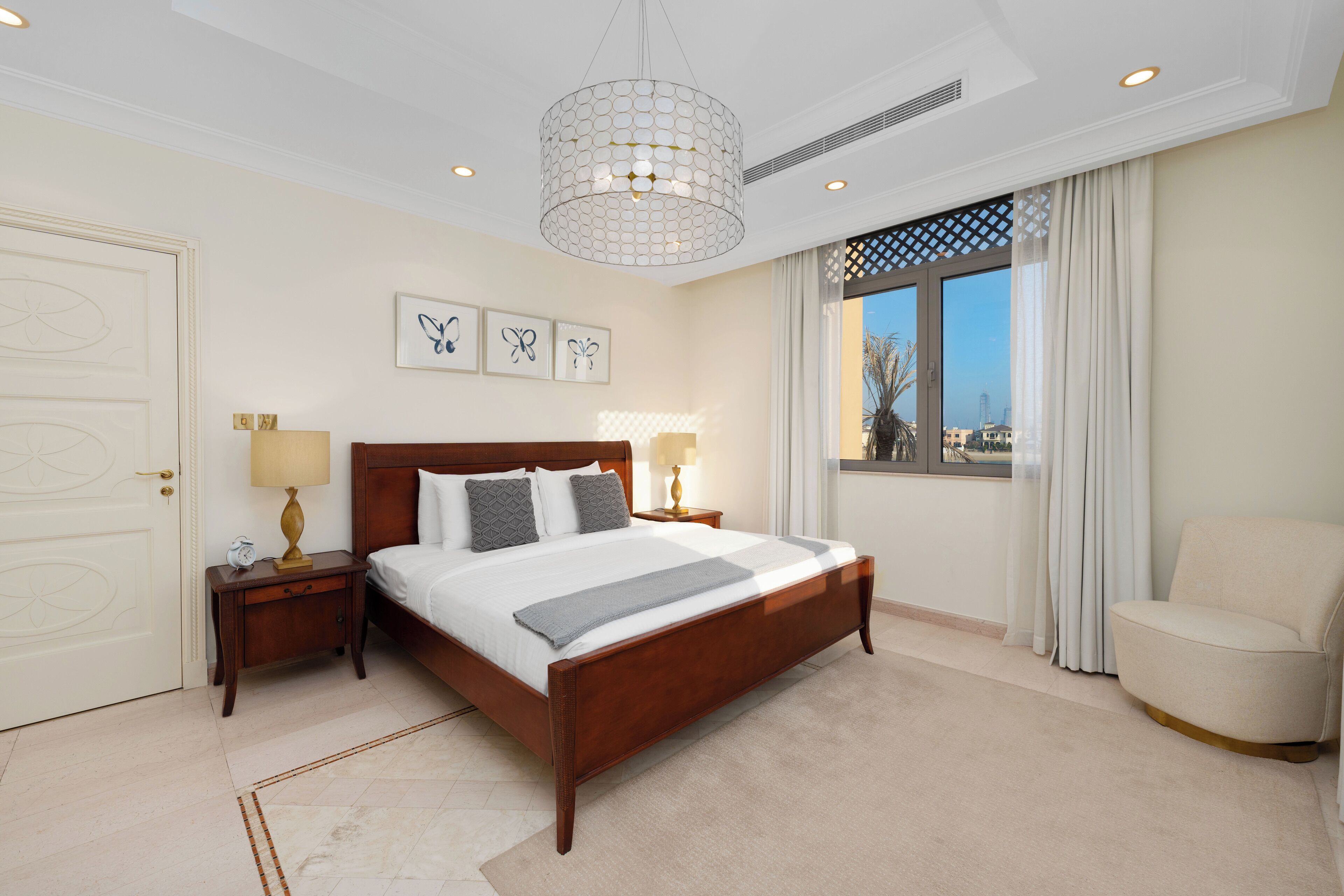 A bedroom with a wooden bed, bedside lamps, a window with curtains, and artwork on the wall.