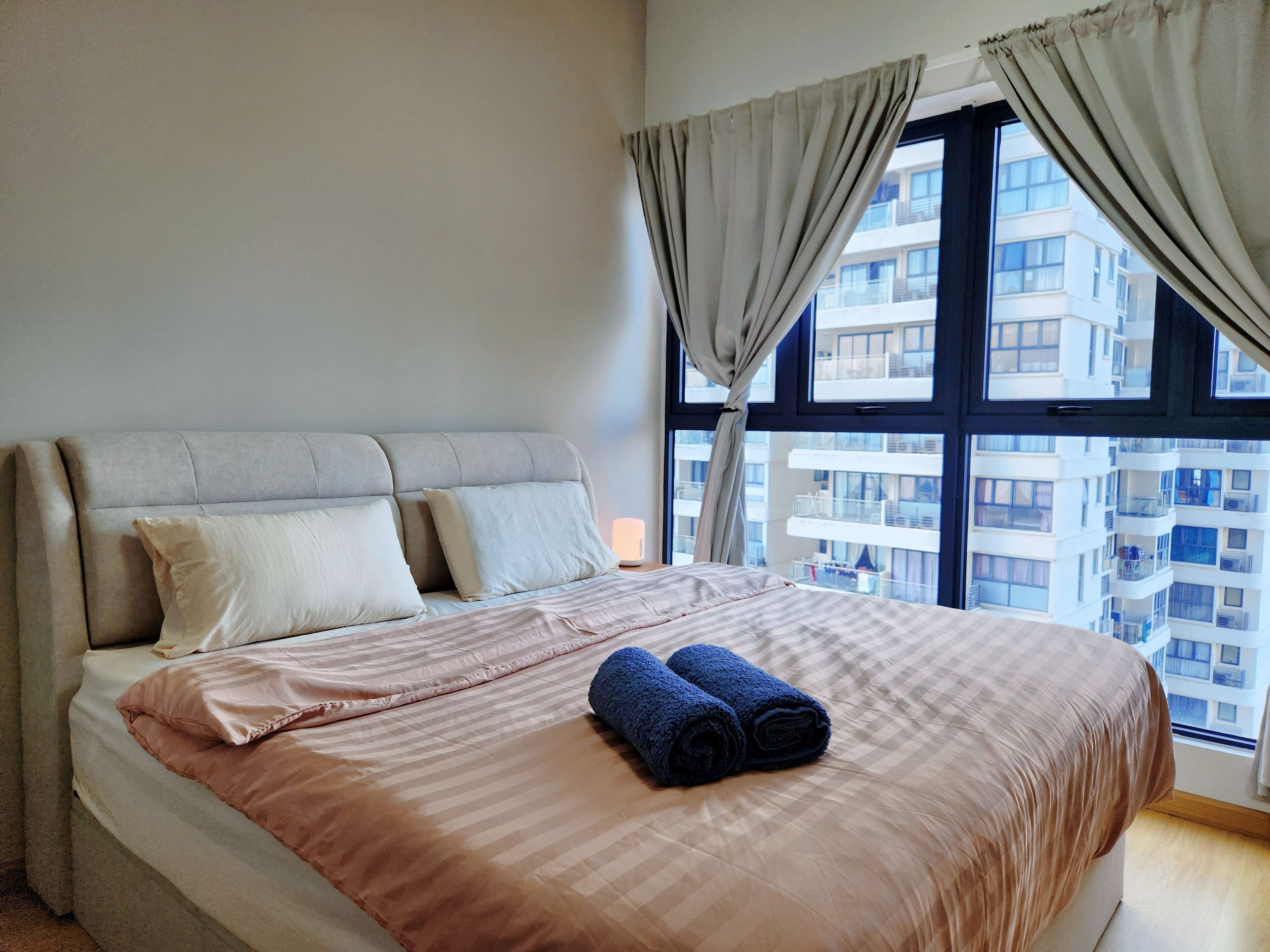 Ein Schlafzimmer mit einem großen Bett, Blick auf ein Gebäude durch das Fenster und einem mit Vorhängen versehenen Fenster.