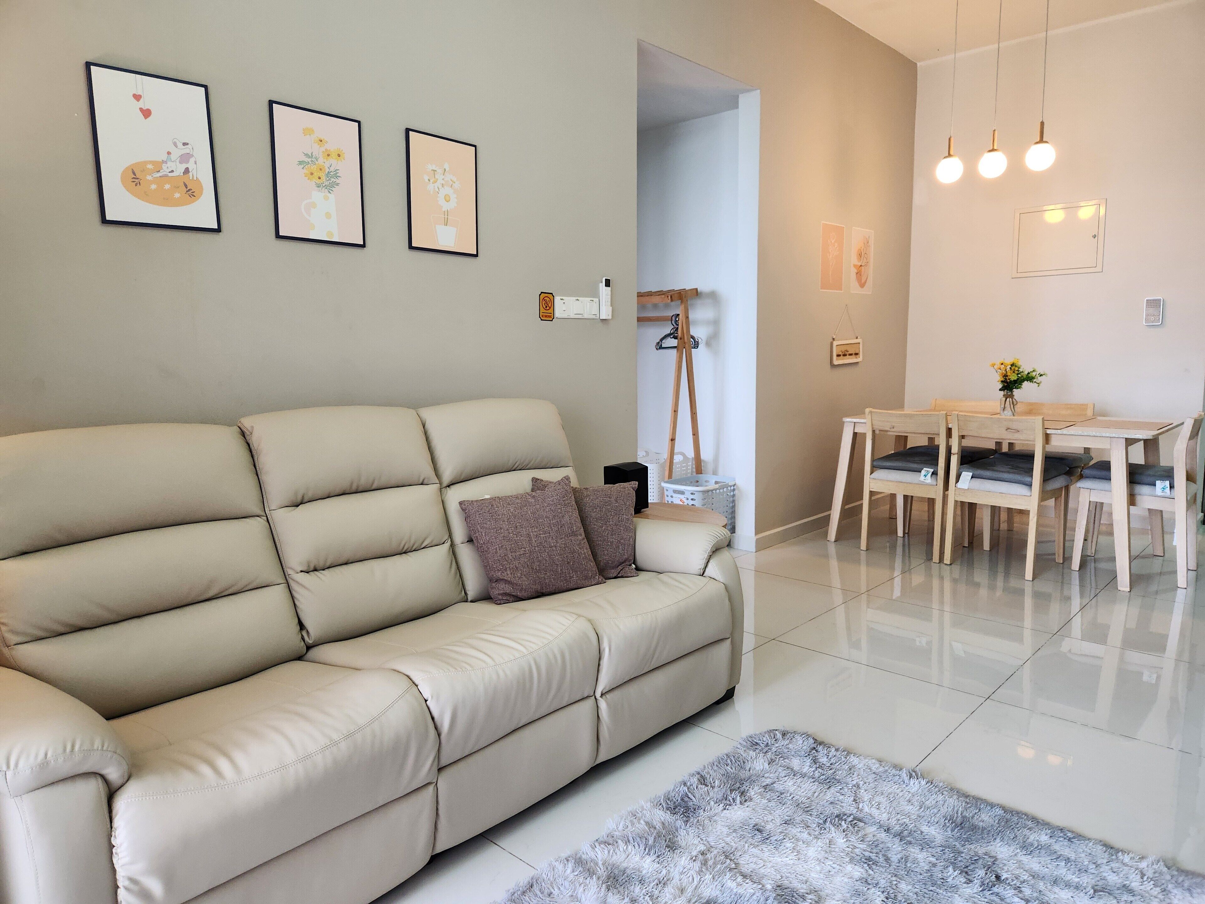 A modern living room with a beige sofa, a small rug, a dining table with chairs, and wall-mounted artwork.