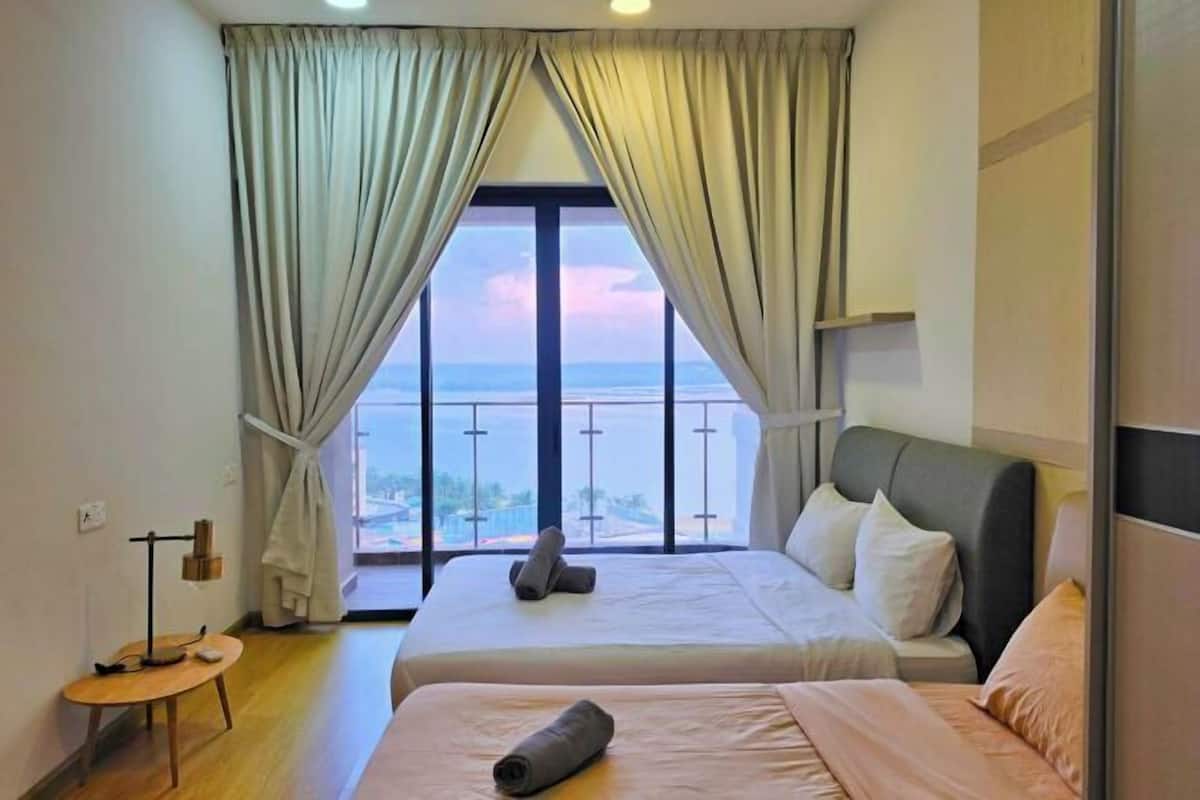 Habitación de hotel con dos camas, una mesita, vista al mar y balcón.