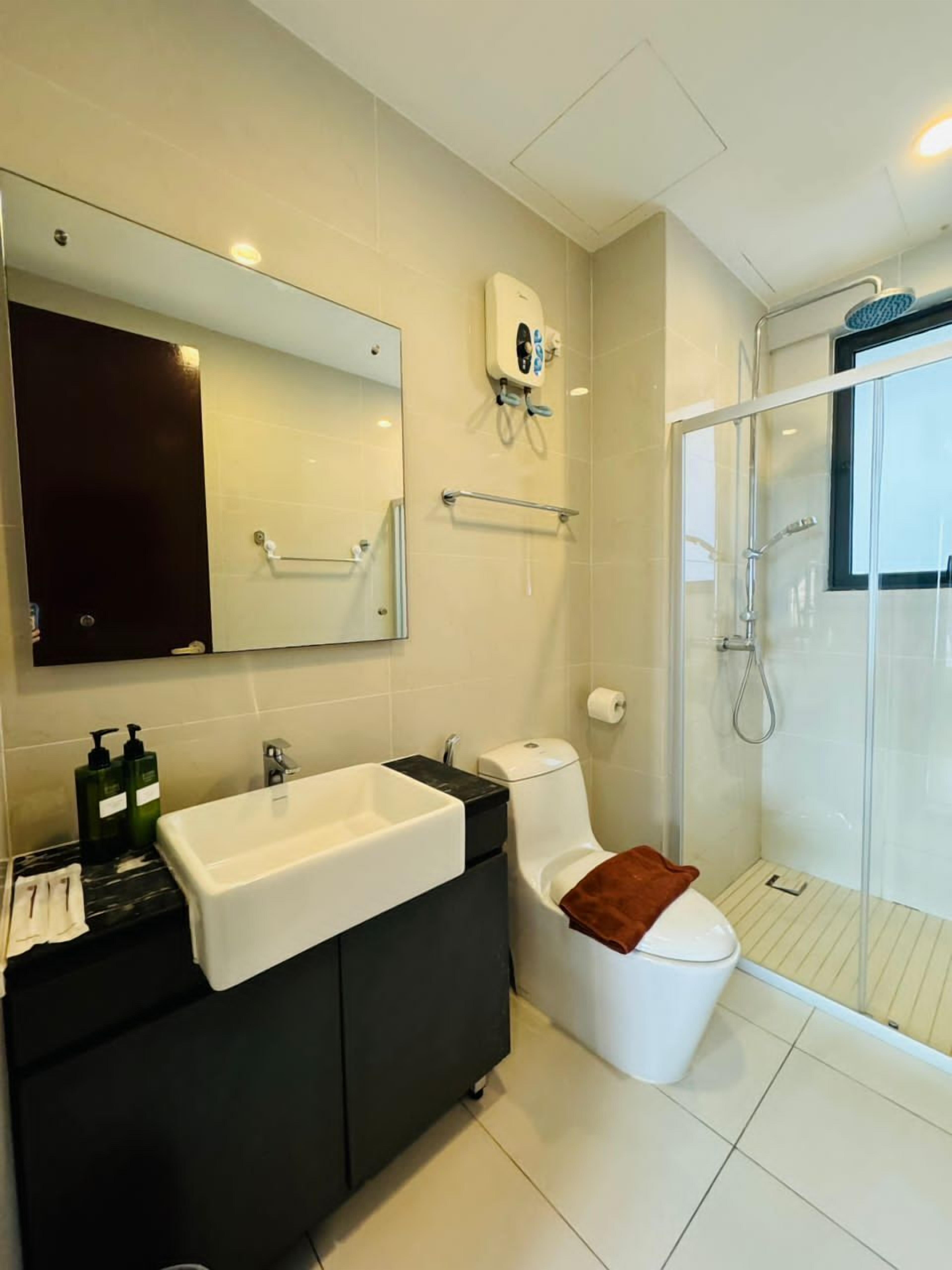 A modern bathroom with a large mirror, a white sink, a black vanity, a toilet, and a glass-enclosed shower.