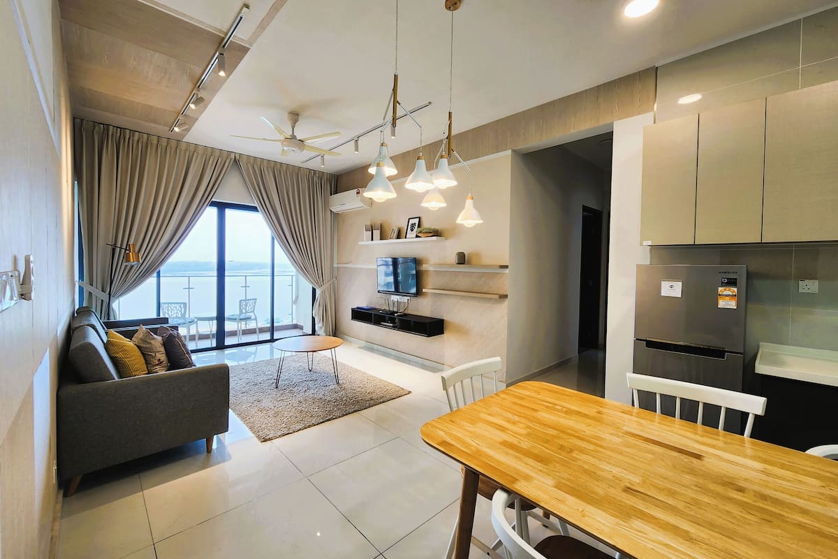 Una sala de estar moderna con sofá, mesa de comedor y área de cocina con refrigerador y armarios.