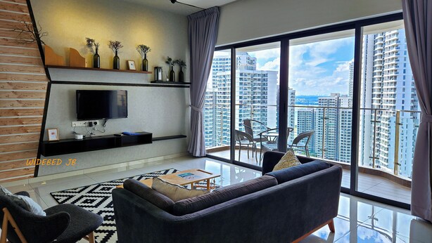 A modern living room with a flat-screen TV, a sofa, and a dining area with a table and chairs. - Country Garden Danga Bay by Widebed JB (Johor Bahru)