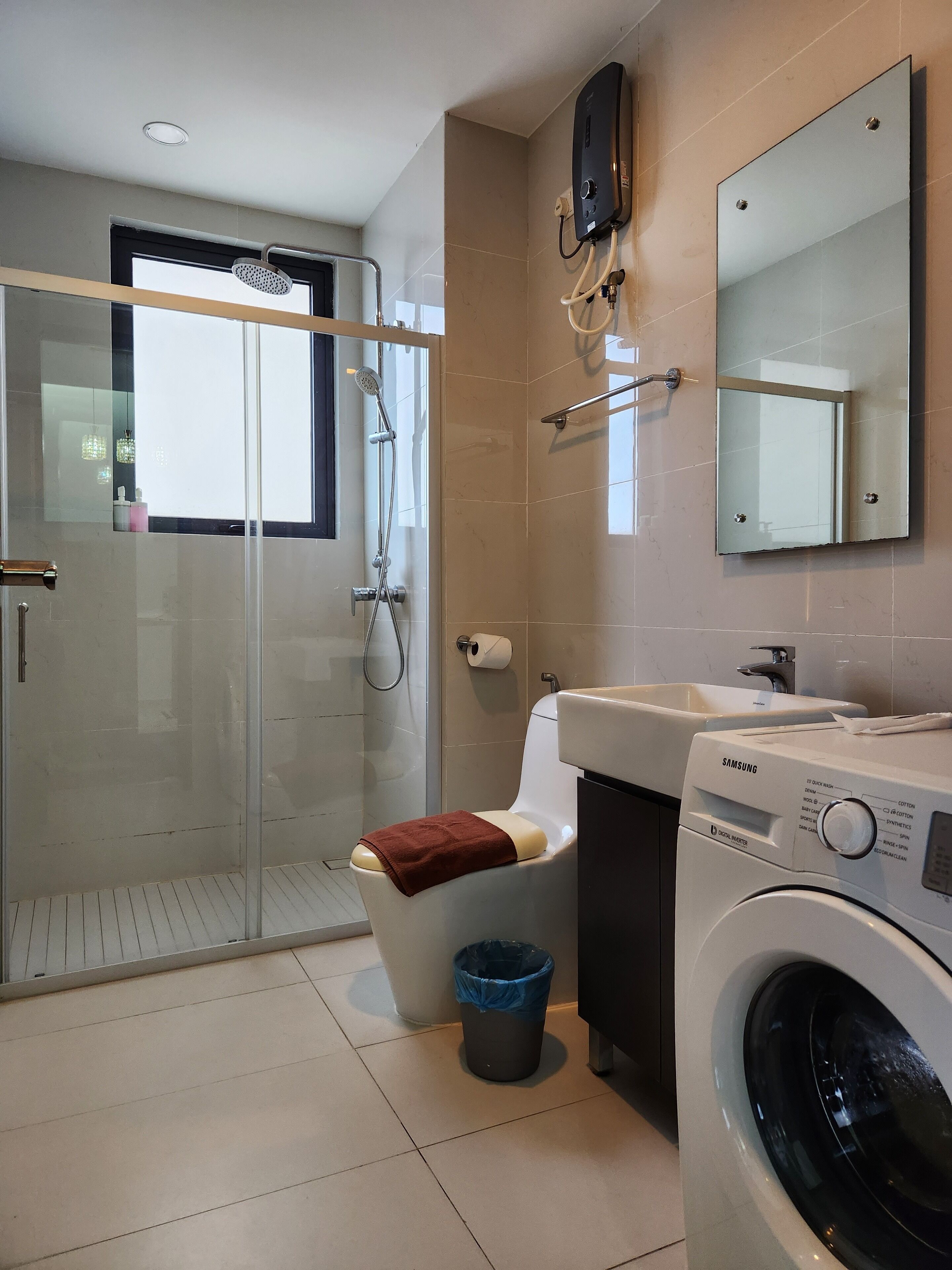 A modern bathroom with a glass shower enclosure, a toilet, a washing machine, and a mirror.
