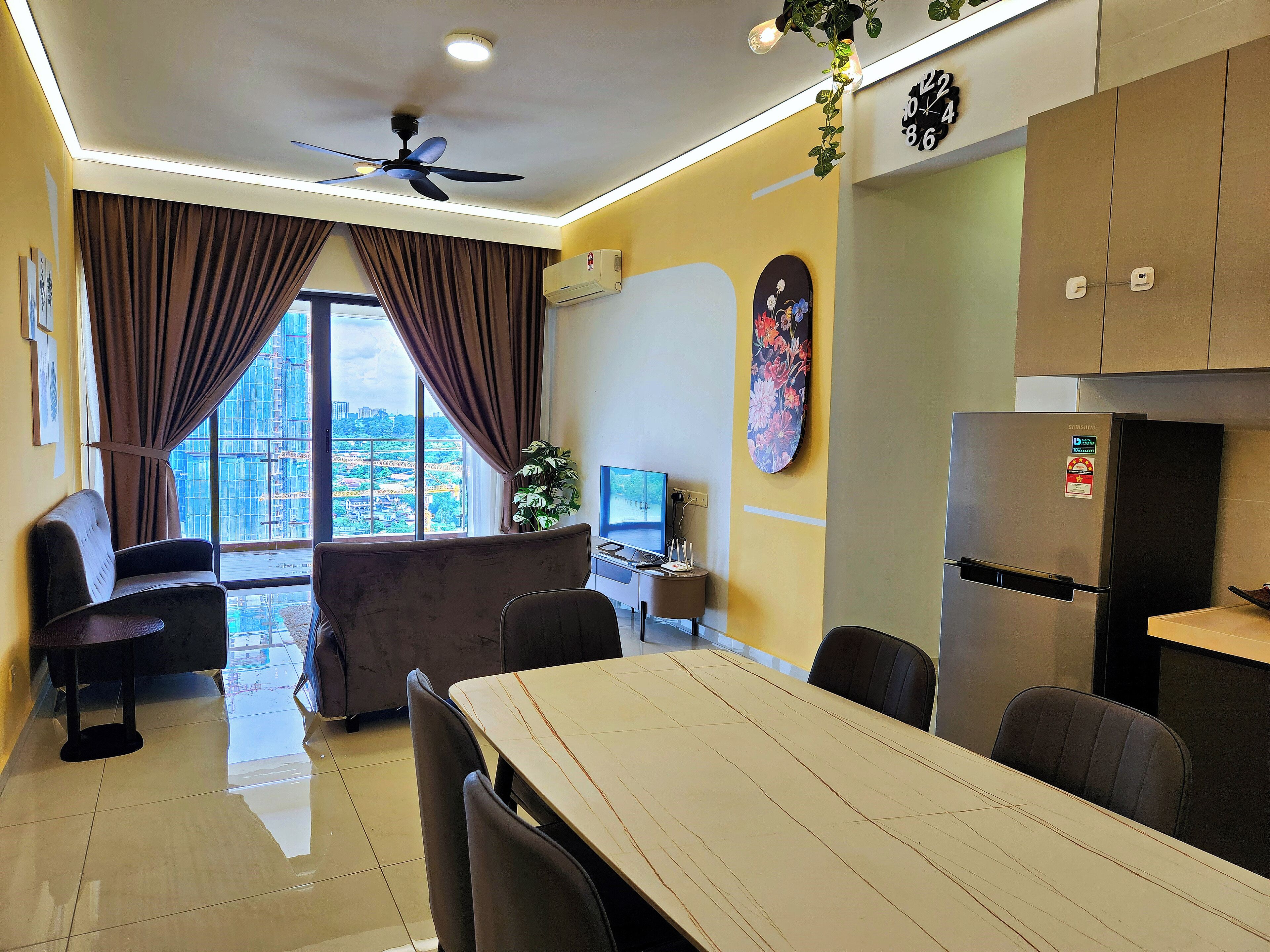 Una sala de estar moderna con comedor, ventanas grandes, ventilador de techo y un refrigerador Samsung.