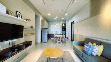 A modern living room with a flat-screen TV, a coffee table, a sofa, and a dining area with chairs.