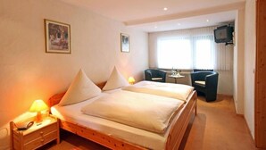 Un dormitorio con una cama de madera, mesitas de noche, un televisor y una ventana con cortinas.