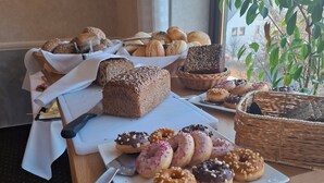 Un bufé de desayuno con diversos panes, bollería y donuts sobre una mesa cerca de una ventana.