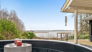 Een jacuzzi met een stenen ondergrond, omgeven door een houten terras en uitzicht op een meer.