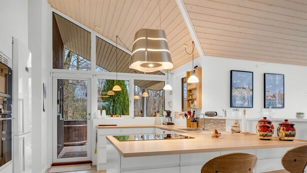 Een moderne keuken met een groot eiland, hangende lampen en uitzicht op de omgeving.