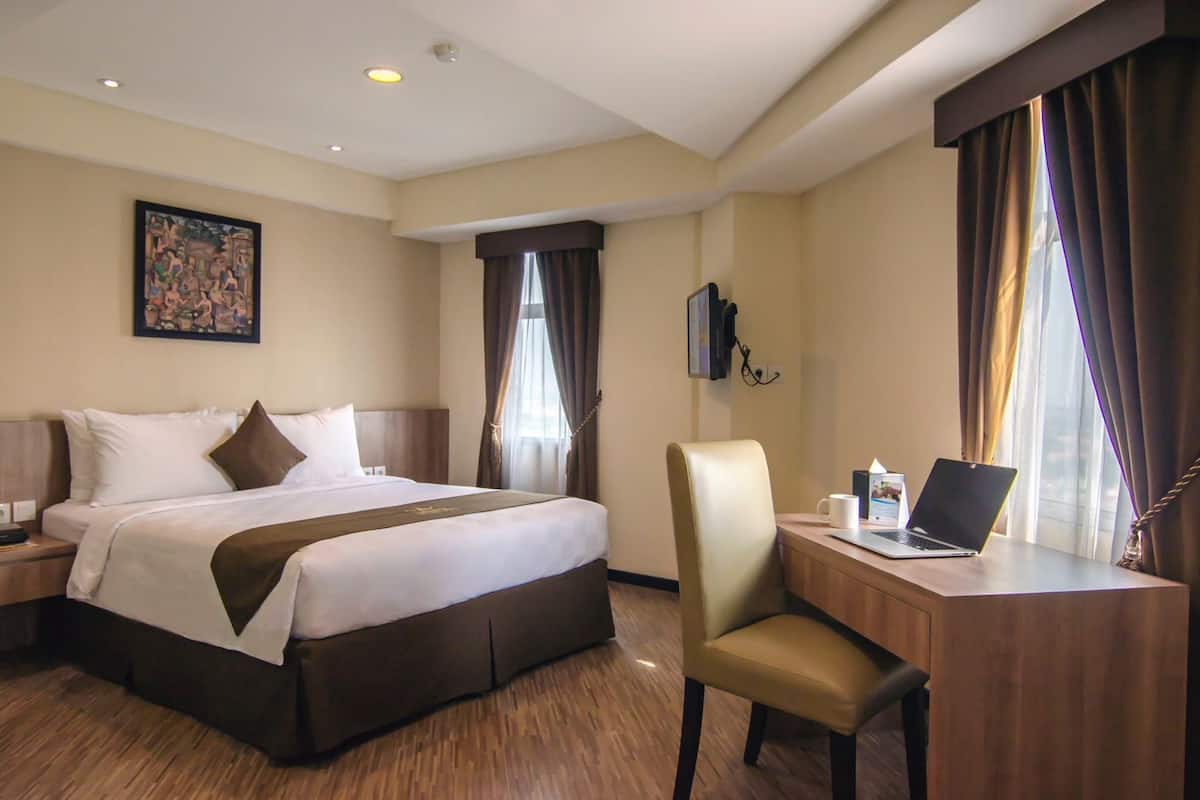 Habitación de hotel con una cama grande, un escritorio con una computadora portátil, una silla y un cuadro en la pared.
