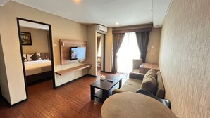 Habitación de hotel con cama, televisor montado en la pared, sofá, mesa de centro y unidad de aire acondicionado.