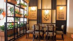 Un área de comedor con una mesa de madera y sillas estampadas, rodeada de estanterías con plantas y decoración mural motivacional.