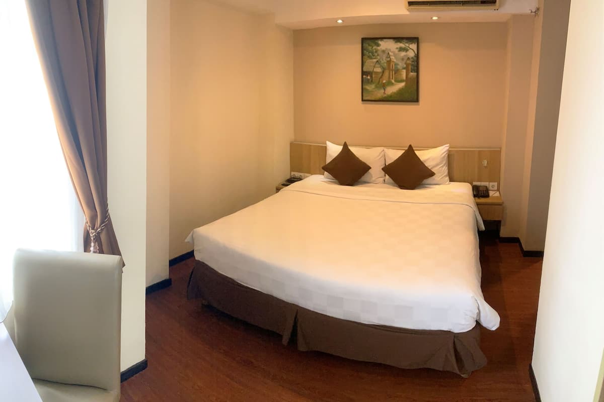 Una habitación de hotel con una cama grande, una mesita de noche, un cuadro en la pared y una silla.