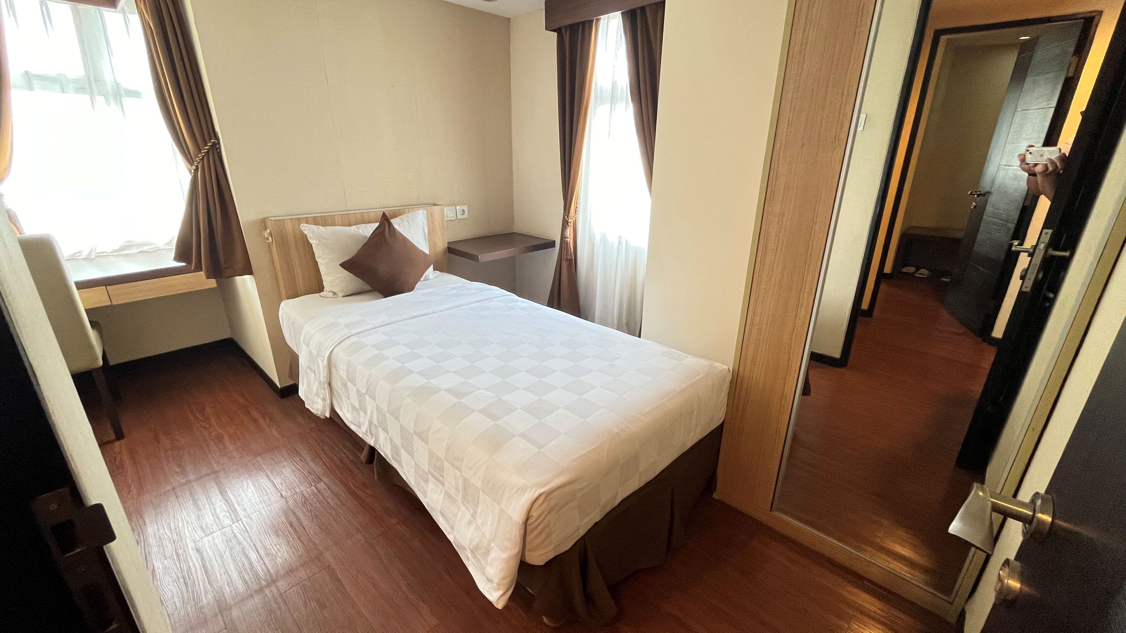 A hotel room with a bed, bedside table, and a window with curtains.