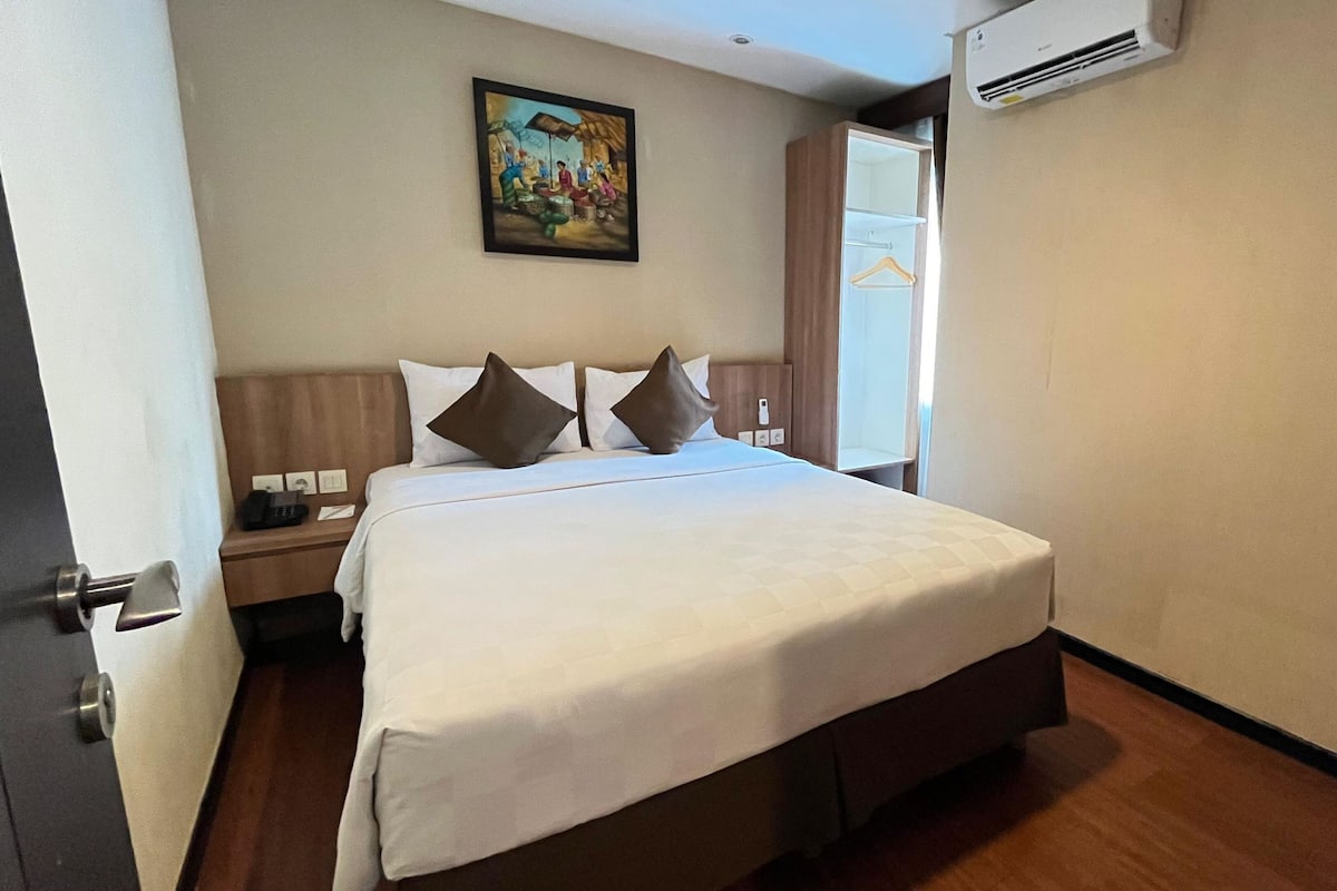 Una habitación de hotel con una cama grande, una mesita de noche, un cuadro en la pared y un equipo de aire acondicionado.