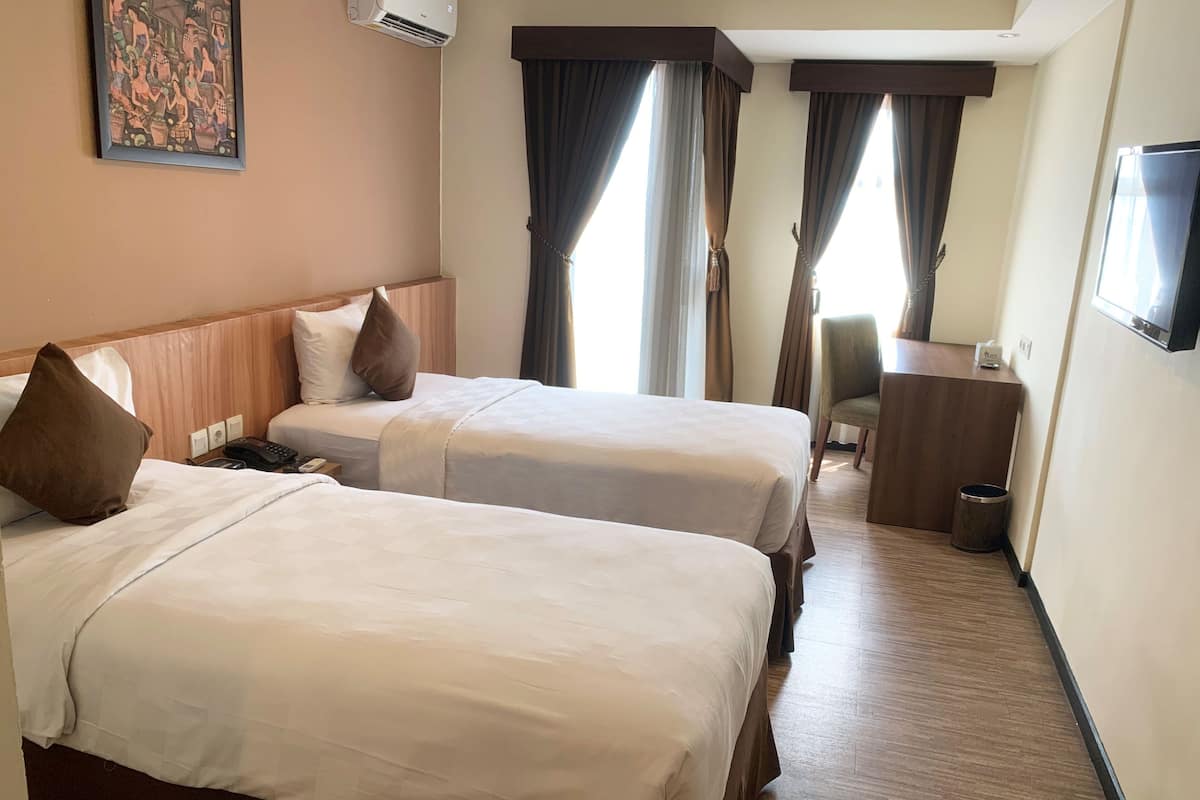 Habitación de hotel con dos camas, un escritorio, una silla, un televisor y un cuadro en la pared.