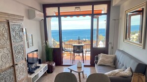 En stue med sofa, fjernsyn, spisebord og balkon med havudsigt.