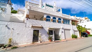 Un edificio blanco de dos pisos con un balcón, un garaje y macetas con plantas.