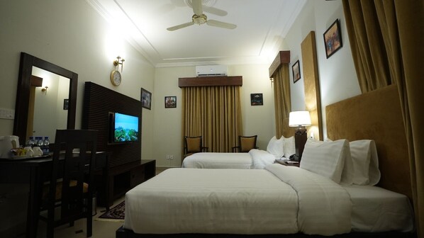 Une chambre d’hôtel avec deux lits, un bureau avec une télévision, un ventilateur de plafond et une fenêtre avec des rideaux.