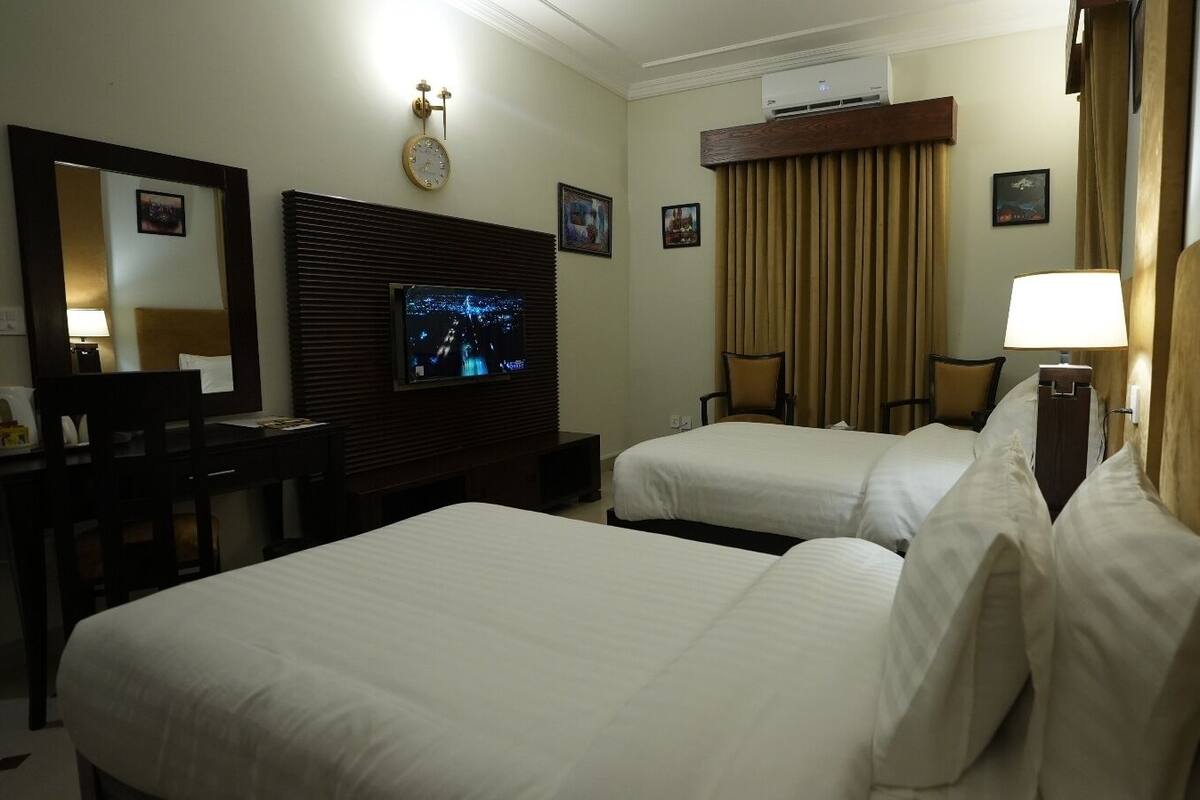 A hotel room with two beds, a TV, a desk, a chair, and a window with curtains.