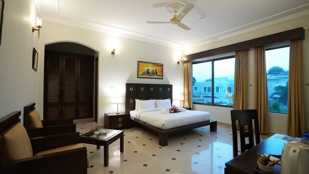 Une chambre d’hôtel avec un lit, un bureau, une chaise, une table de chevet, une lampe et une vue sur l’extérieur.
