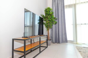 A modern living room with a flat-screen TV on a wooden and metal console table, a potted plant, and a large window with curtains.