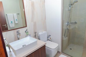 Enjoy a refreshing shower in the spacious bathroom with a large sink, toilet, and glass-enclosed shower area.