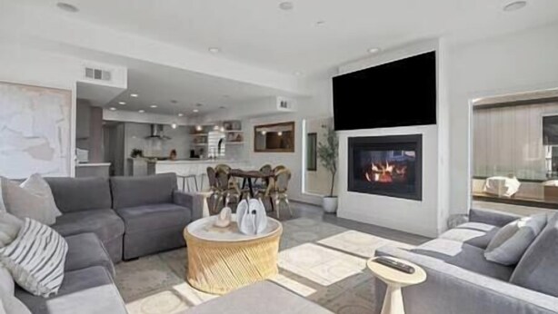 Una sala de estar moderna con chimenea, sofás grises y una cocina al fondo.