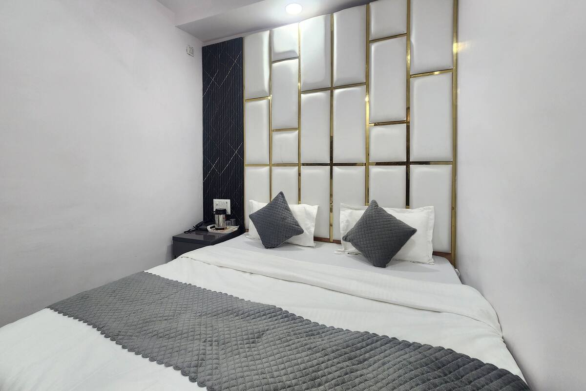 A modern bedroom with a tufted headboard, a bedside table with a lamp, and a grey quilted throw blanket.