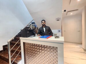 A hotel reception desk with a printer, a blue folder, and a sign that reads "Cottage Yes Sir". - Cottage Yes Sir Dx (New Delhi)