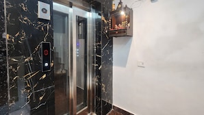 An elevator with a digital display, marble walls, and a small shelf with decorative items. - Cottage Yes Sir Dx (New Delhi)