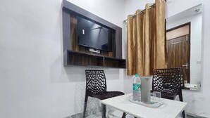 A small room with a TV mounted on the wall, two chairs, a table with a bottle and glasses, and a door with a mirror. - Cottage Yes Sir Dx (New Delhi)