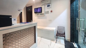 A modern hotel room with a reception desk, a television, an air conditioning unit, and a glass shower enclosure. - Cottage Yes Sir Dx (New Delhi)