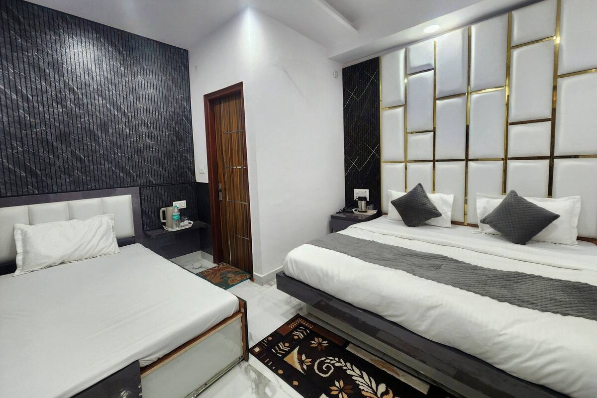 A modern hotel room with two beds, a wooden door, a nightstand with a coffee maker, and a decorative wall panel.