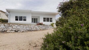 A modern white house with a stone retaining wall and a sandy driveway.