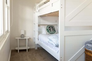Una cama individual con un cojín del logo de Starbucks, una mesita de noche con una lámpara y una ventana.
