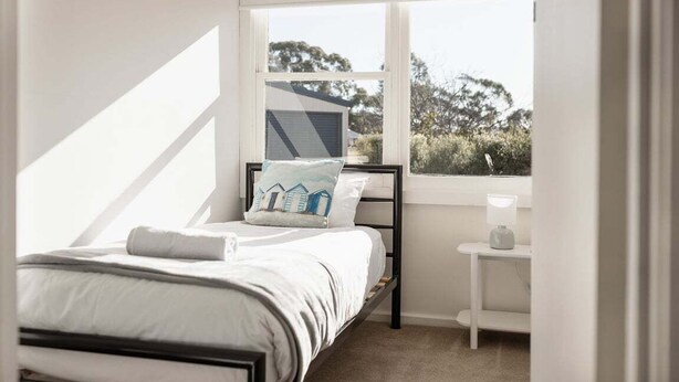 A bedroom with a bed, a nightstand, a window, and a view of trees.