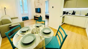 Een moderne woonkamer met een eettafel voor vier personen, een bank, een televisie en een keuken met een aanrecht en gootsteen.
