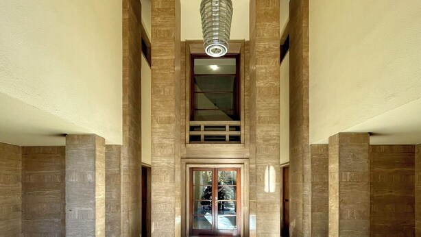 Een ruime lobby met marmeren vloeren, hoge houten zuilen en een moderne verlichtingsarmatuur.