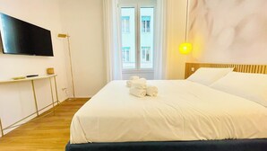 Een hotelkamer met een bed, een aan de muur bevestigde televisie, een nachtkastje en een raam met gordijnen.