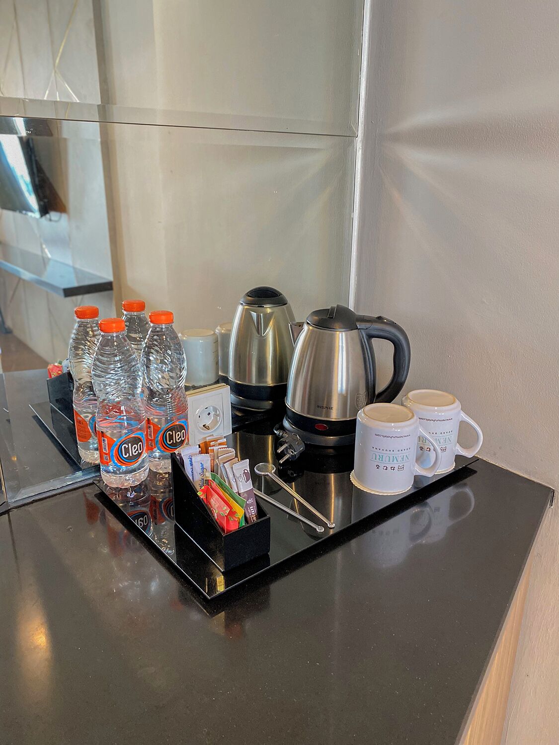 Minibar de una habitación de hotel con agua embotellada, cafeteras y tazas.