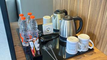 Une kitchenette dans une chambre d’hôtel, équipée d’un plan de travail en bois, d’une bouilloire, d’une machine à café et de plusieurs bouteilles d’eau.