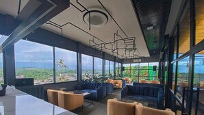 A modern lounge area with seating and a bar, large windows offering a city view. - Nemuru Grand Bhuvana Ciawi (Ciawi)