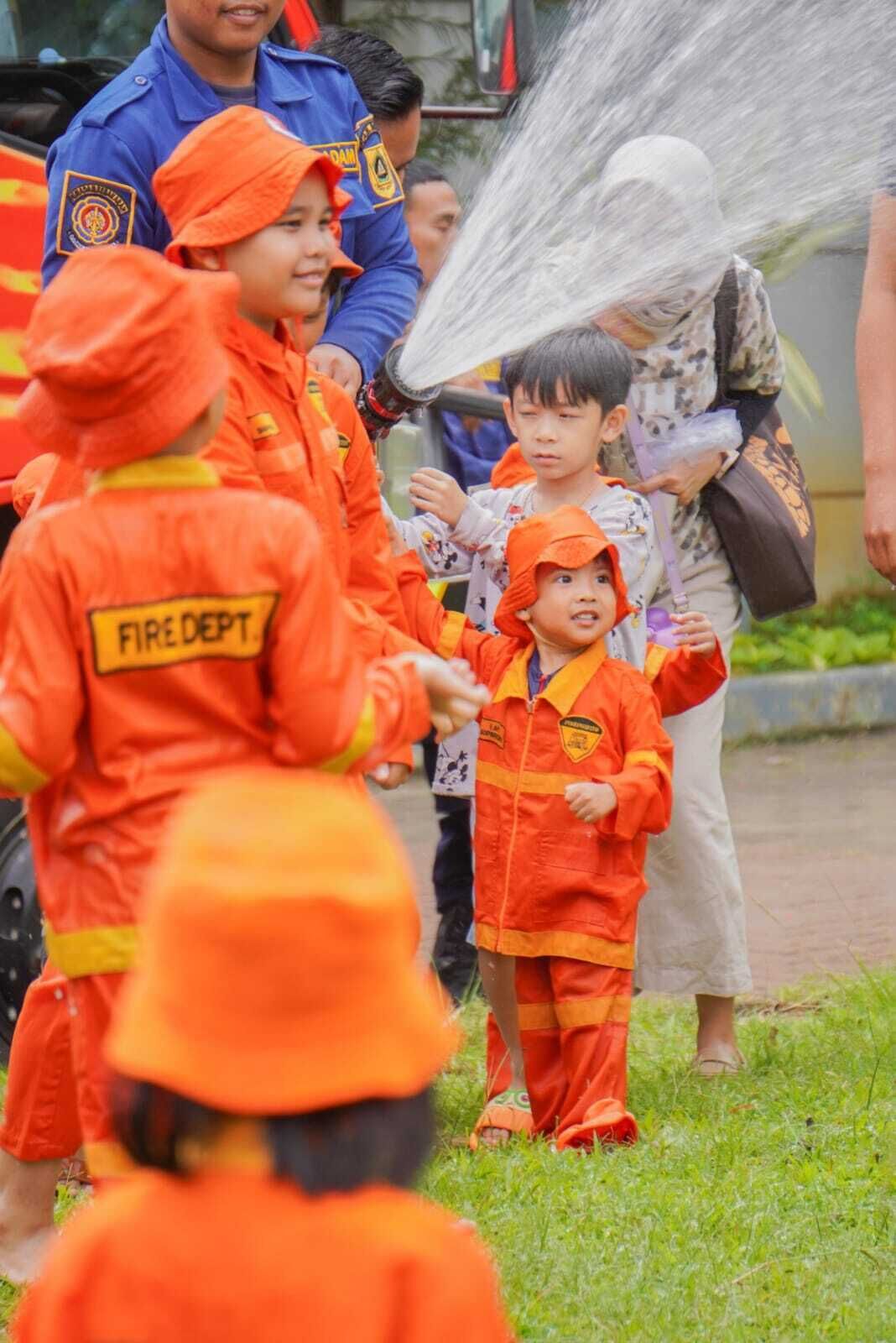 Children in orange uniforms with 'FIRE DEPT' on the back, participating in an outdoor activity.