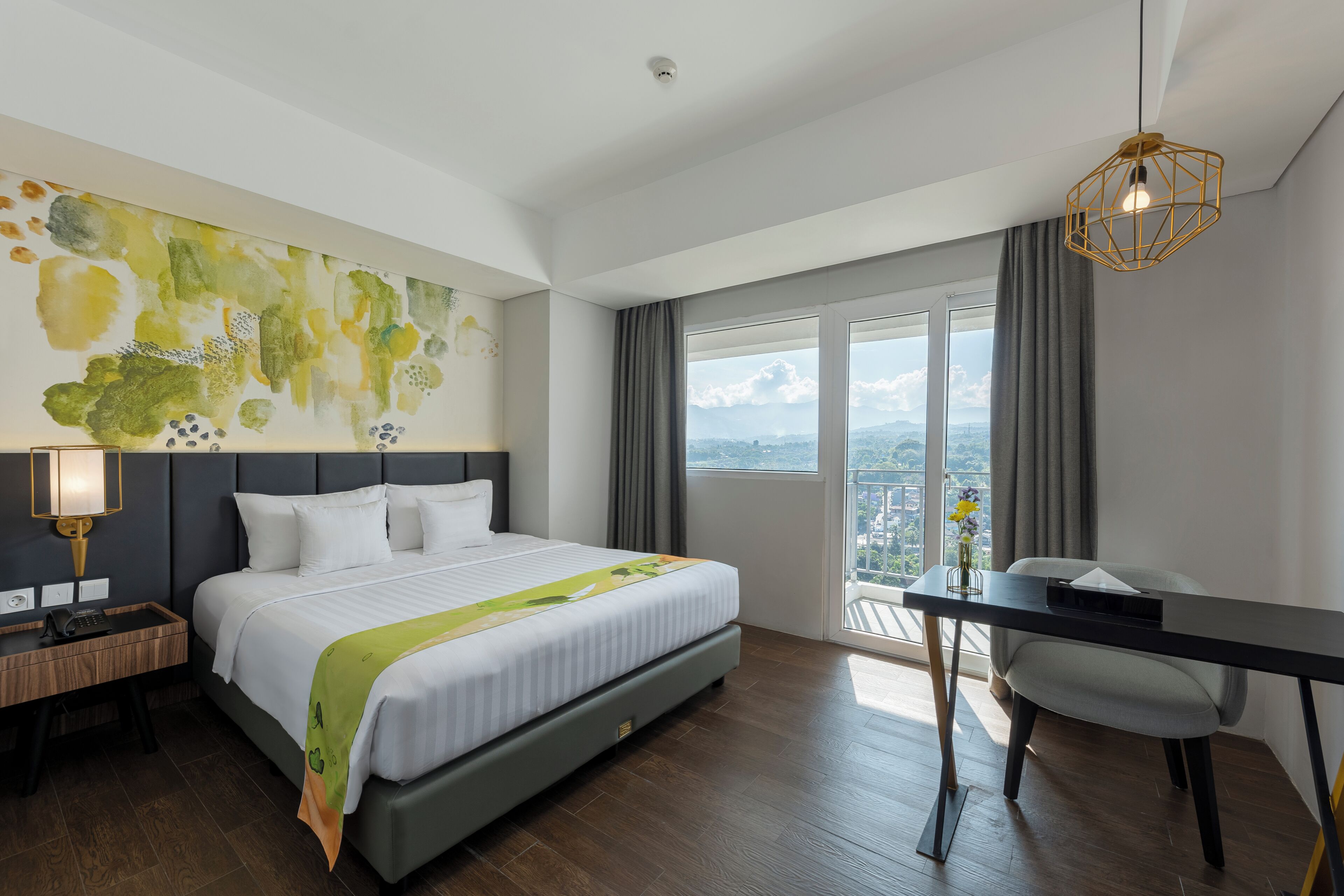 Habitación de hotel con una cama grande, un escritorio, una silla, vistas a la ciudad y una lámpara moderna.