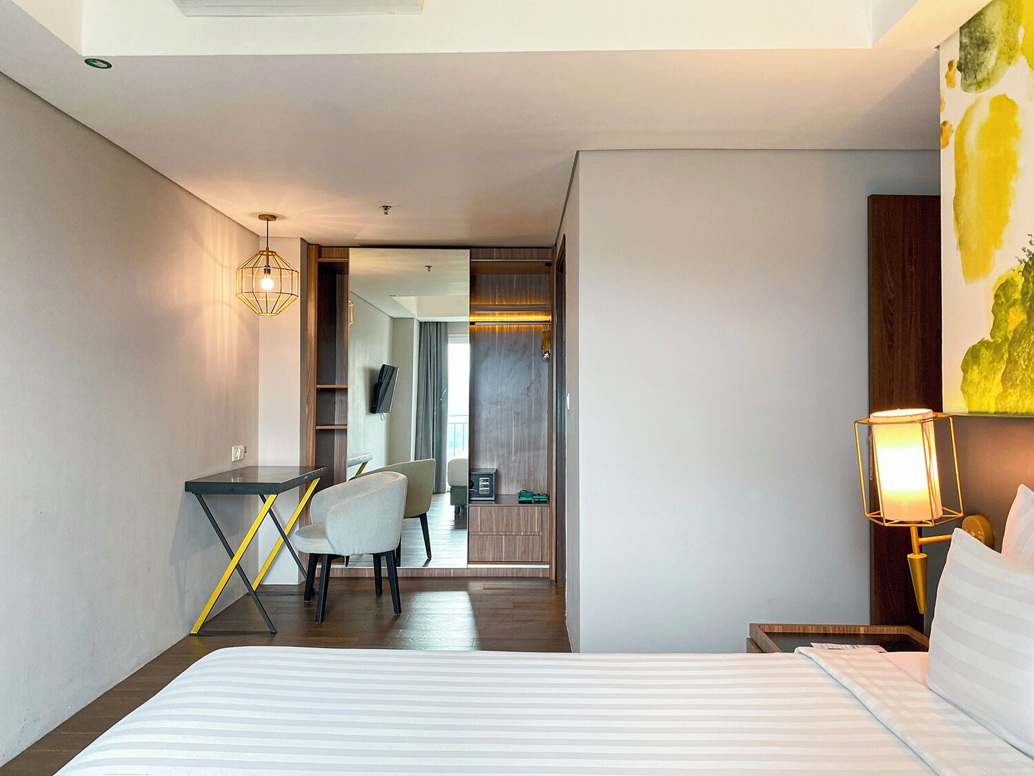 A hotel room with a bed, a desk with a chair, a television, and a painting on the wall.