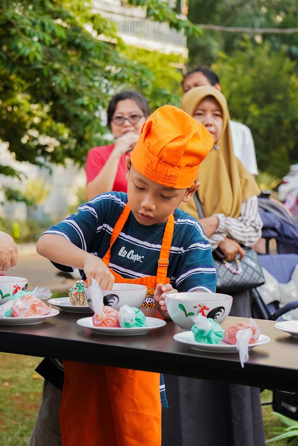 A person wearing an orange chef's hat and apron, preparing food at an outdoor event.