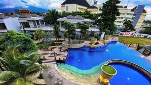 A large, curved swimming pool with a blue center, surrounded by lounge chairs and a stone pathway. - Nemuru Grand Bhuvana Ciawi (Ciawi)